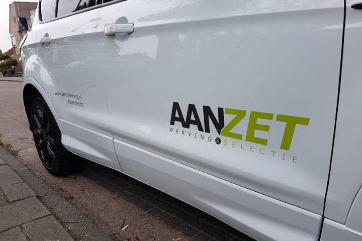 Het logo van Aanzet op de autodeur